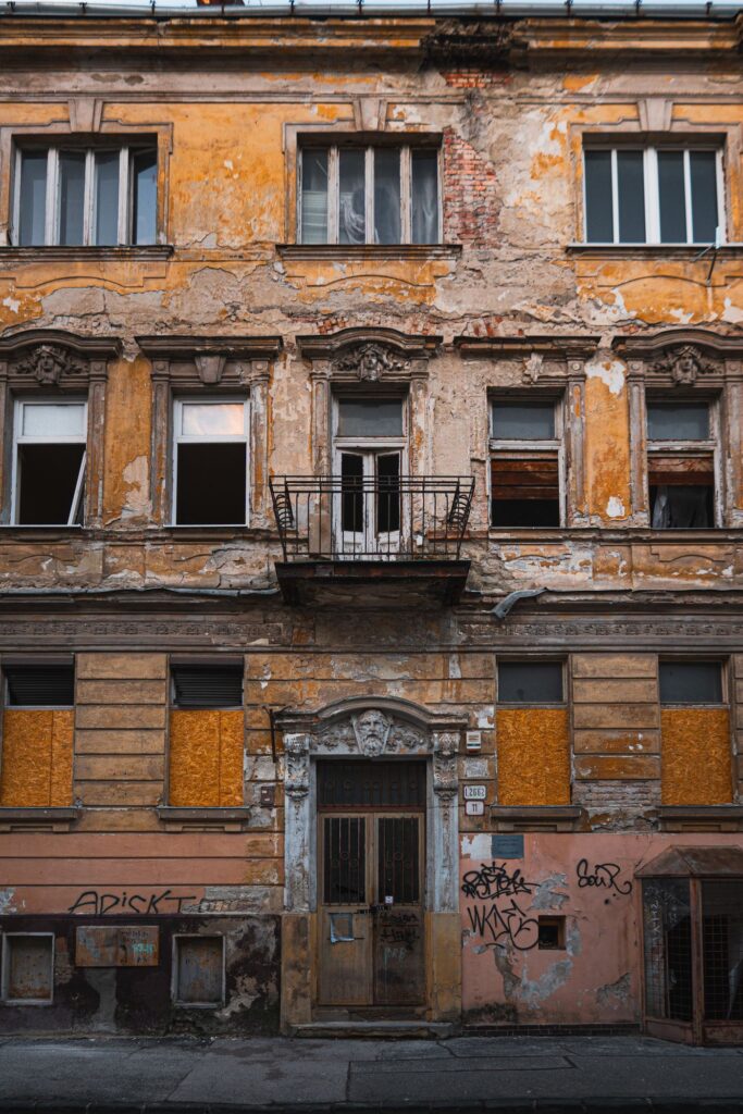 A decayed building facade with peeling plaster and boarded windows
