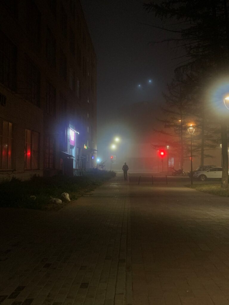 A foggy city street at night with distant traffic lights