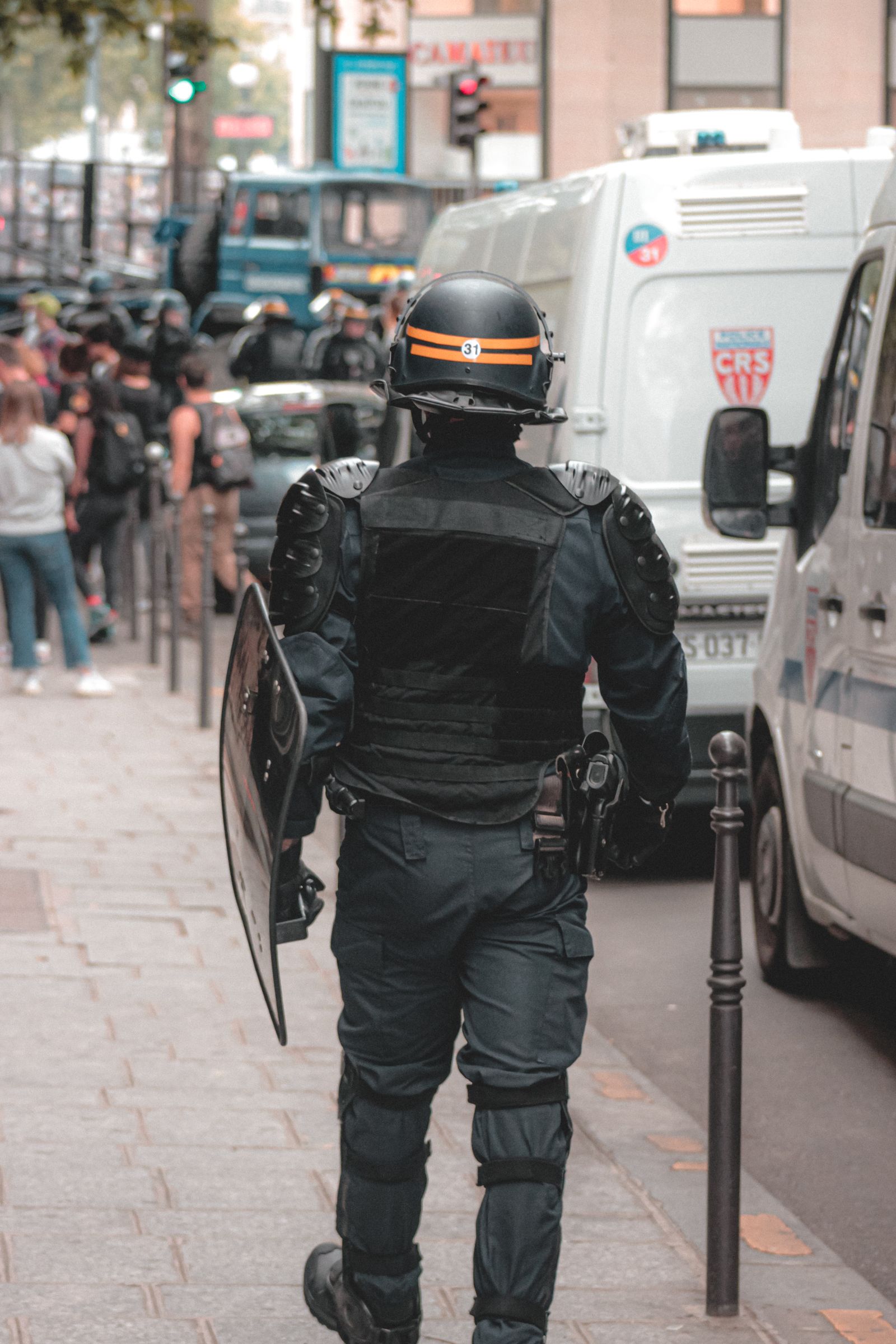 Riot police officer seen from behind walking along a street toward a crowd