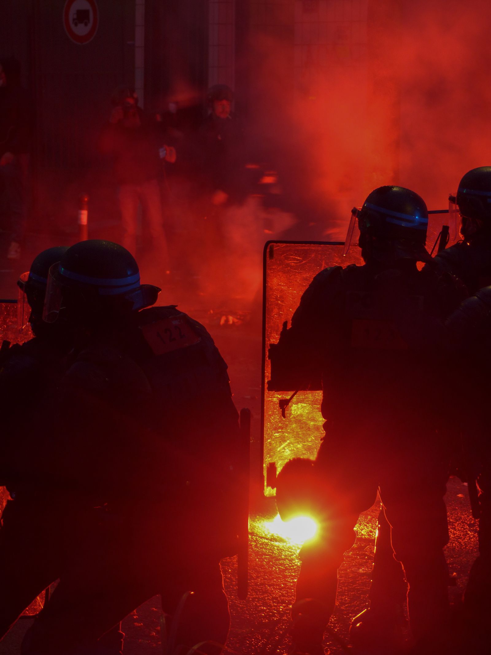 Silhouetted police officers with shields in red smoke during a night protest
